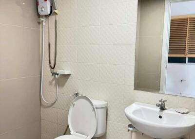 Compact bathroom with white fixtures, including a toilet, sink, and shower with water heater