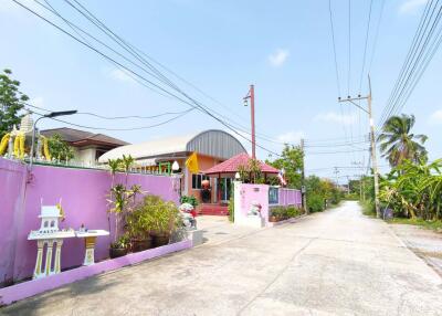 Colorful single-story residential building with a pink fence and tropical surroundings