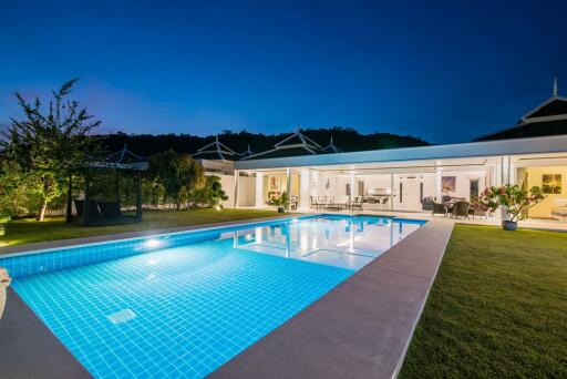 Elegant outdoor pool area with well-lit house and garden at dusk