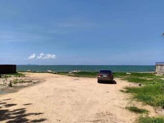 Unpaved coastal land with a parked car and sea view under a clear blue sky