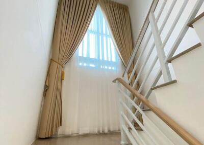 Modern staircase with white steps, metal handrails, and a sizable window with curtains