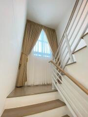 Modern staircase with white steps, metal handrails, and a sizable window with curtains