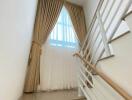 Modern staircase with white steps, metal handrails, and a sizable window with curtains