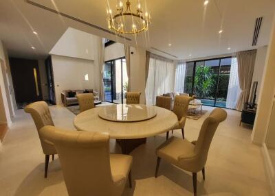 Elegant dining room with a round table and comfortable chairs, well-lit with natural lighting and modern chandelier