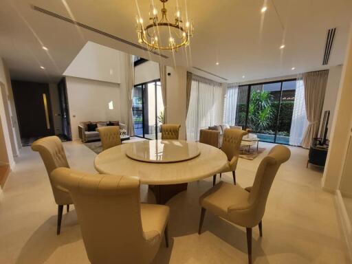 Elegant dining room with a round table and comfortable chairs, well-lit with natural lighting and modern chandelier