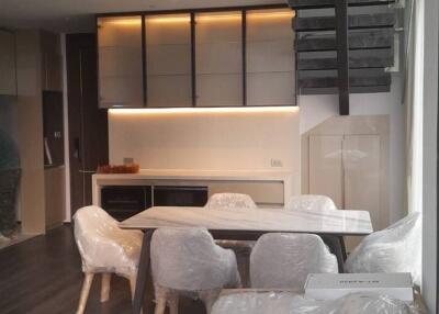 Modern kitchen with white cabinetry and a dining area with a table and chairs covered in protective plastic