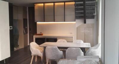 Modern kitchen with white cabinetry and a dining area with a table and chairs covered in protective plastic