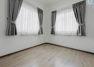 Empty bedroom with hardwood floors and two windows with curtains