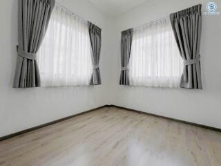 Empty bedroom with hardwood floors and two windows with curtains