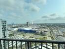 City skyline view from a high-rise balcony with clear railings overlooking a busy urban area with prominent buildings and parking lots