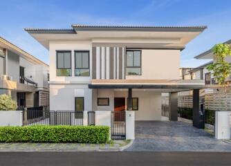 Modern two-story house with a flat roof, carport, and landscaped garden