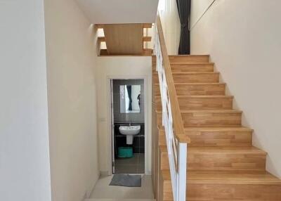 Wooden staircase with white railing leading to upper floor with a small bathroom visible underneath