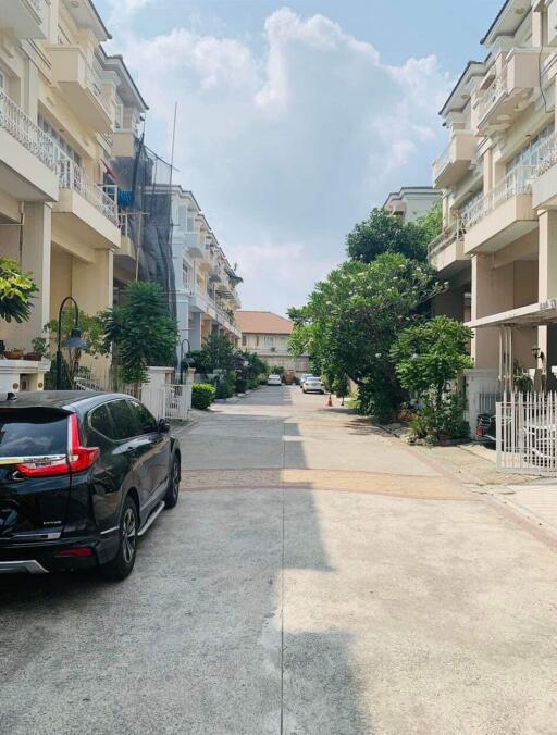 Quiet residential street lined with townhouses and parked car under a bright sky