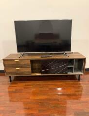 Modern living room with a large flat-screen TV and wooden media console on polished hardwood floor