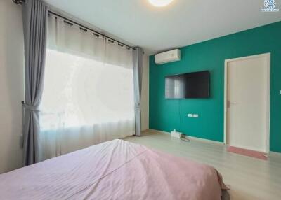 Bright and modern bedroom with teal walls, large window, and mounted television