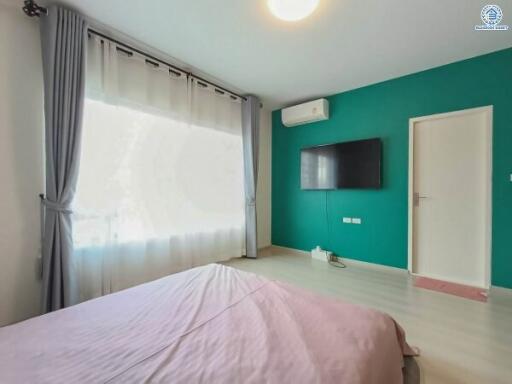 Bright and modern bedroom with teal walls, large window, and mounted television