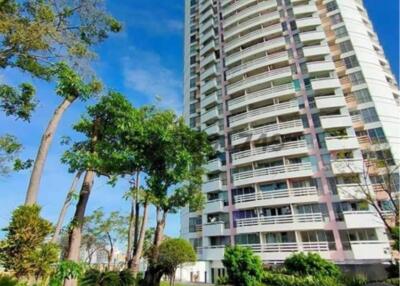 High-rise residential building surrounded by greenery under clear blue sky