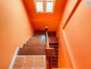 Brightly lit staircase with orange walls leading to an upper level