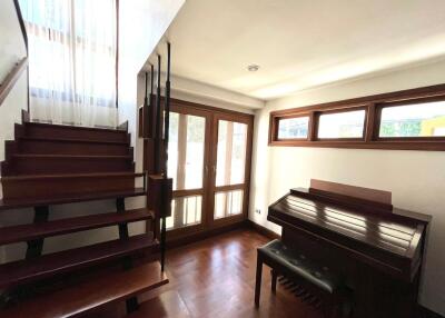 Spacious living room with natural lighting, wooden staircase, and a piano
