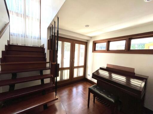 Spacious living room with natural lighting, wooden staircase, and a piano