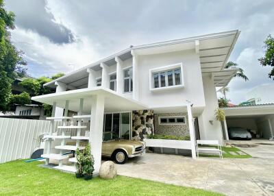 Modern white two-story house with a lush green lawn and a vintage car parked under the carport