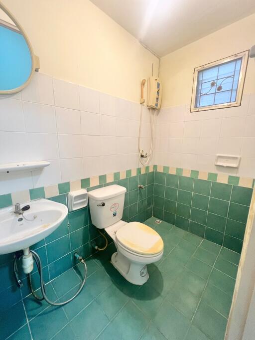 Compact bathroom with white and green tiles, wall-mounted sink, and toilet