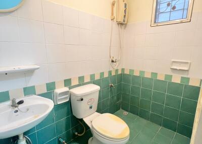 Compact bathroom with white and green tiles, wall-mounted sink, and toilet