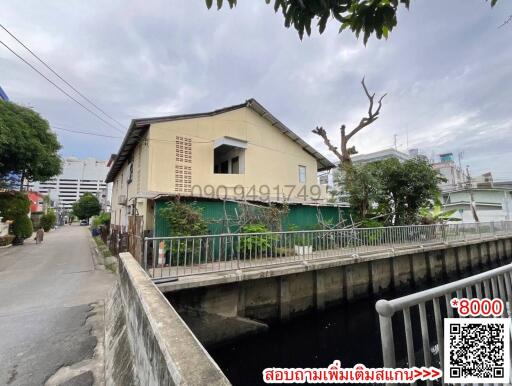 Exterior view of a two-story house by a canal with surrounding greenery