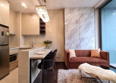 Modern kitchen with stainless steel appliances adjacent to cozy living space with a brown sofa and a chic fur-covered chair