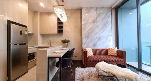 Modern kitchen with stainless steel appliances adjacent to cozy living space with a brown sofa and a chic fur-covered chair