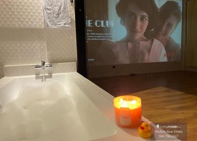 Cozy bathtub with a lit candle and entertainment screen in modern bathroom