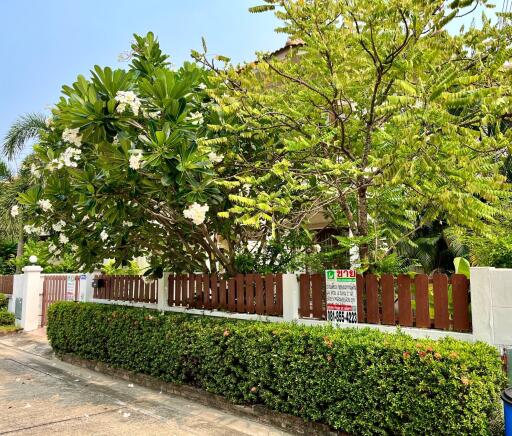 Lush green front yard with private fencing and a visible for-sale sign