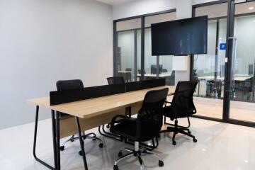 Modern conference room with large wooden table, black chairs, and a flat-screen TV