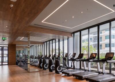 Modern gym interior with treadmills, exercise bikes, and large windows showing urban views