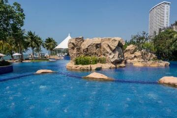 Resort-style outdoor swimming pool with lush landscaping, rocks, and nearby beach