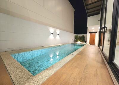 Elegant outdoor swimming pool area with wooden deck and modern lighting at night