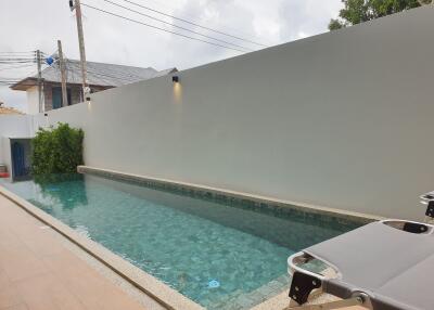 Modern private outdoor swimming pool with high privacy walls and elegant lounging chairs