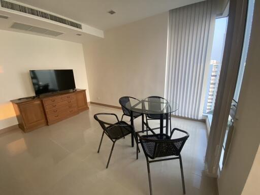 Modern living room with natural light, featuring a glass dining table and a large TV