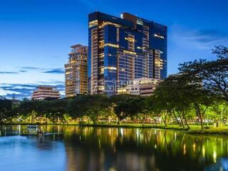 Modern high-rise residential building illuminated at twilight with a foreground of a serene park and reflective pond