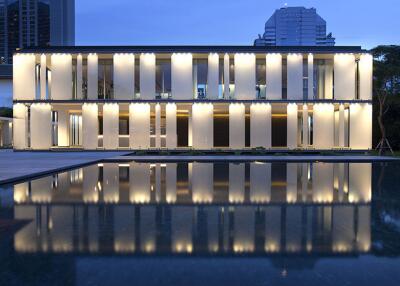 Modern architectural building exterior with illuminated facade and reflexive pool at twilight
