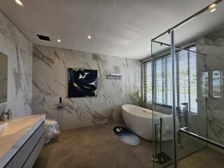 Modern bathroom with marble walls, freestanding tub, and glass shower