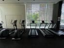 Modern condo gym with various workout equipment facing large windows