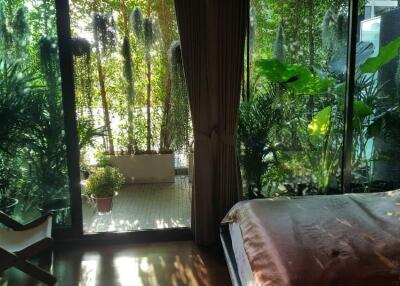 Cozy bedroom with a view of lush greenery through floor-to-ceiling windows