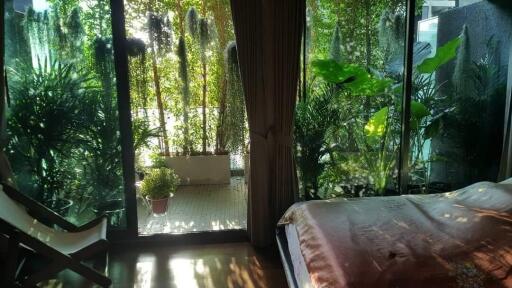 Cozy bedroom with a view of lush greenery through floor-to-ceiling windows