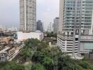 Cityscape view from a high-rise apartment showing multiple buildings and greenery