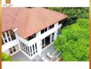 Aerial view of a spacious two-story residential house with terracotta roof tiles surrounded by lush greenery