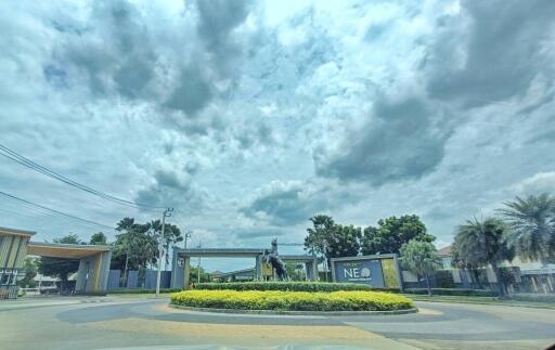 Cloudy sky over a gated community entrance with landscaped roundabout