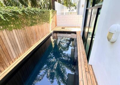 Narrow outdoor pool with wooden decking surrounded by trees