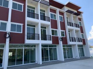 Modern red and white apartment building with spacious balconies and ground floor commercial spaces