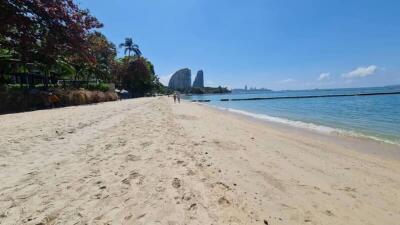 Serene beachfront with clear skies, sandy shores, and lush greenery near residential high-rises